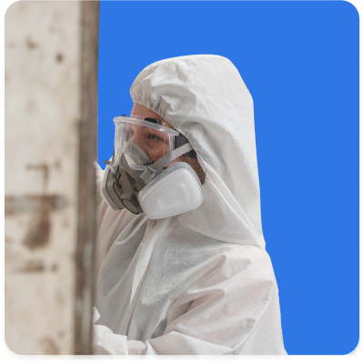 Person in protective gear, including a white suit, goggles, and a respirator mask, working. Blue background highlights the importance of proper safety measures and asbestos liability insurance in hazardous environments.