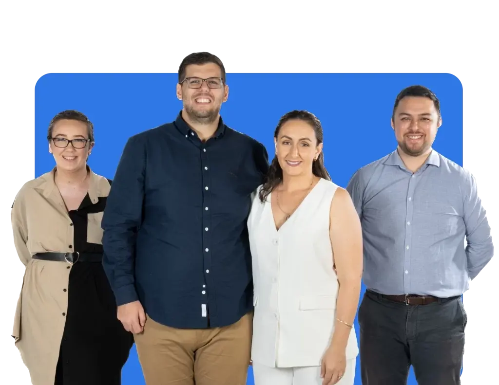 Four people standing and smiling in front of a blue background. The group consists of a woman in a beige coat, a man in a dark shirt, a woman in a white outfit, and a man in a light shirt.
