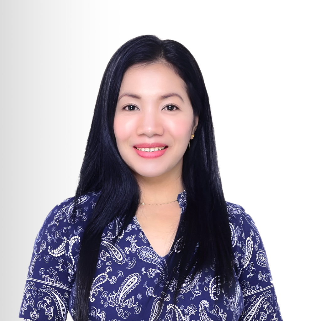 A woman with long black hair wearing a blue paisley patterned shirt smiles at the camera against a white background.